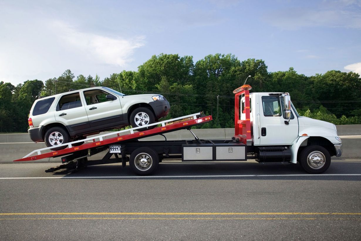 White SUV on a red flatbed tow truck on a road with trees in the background