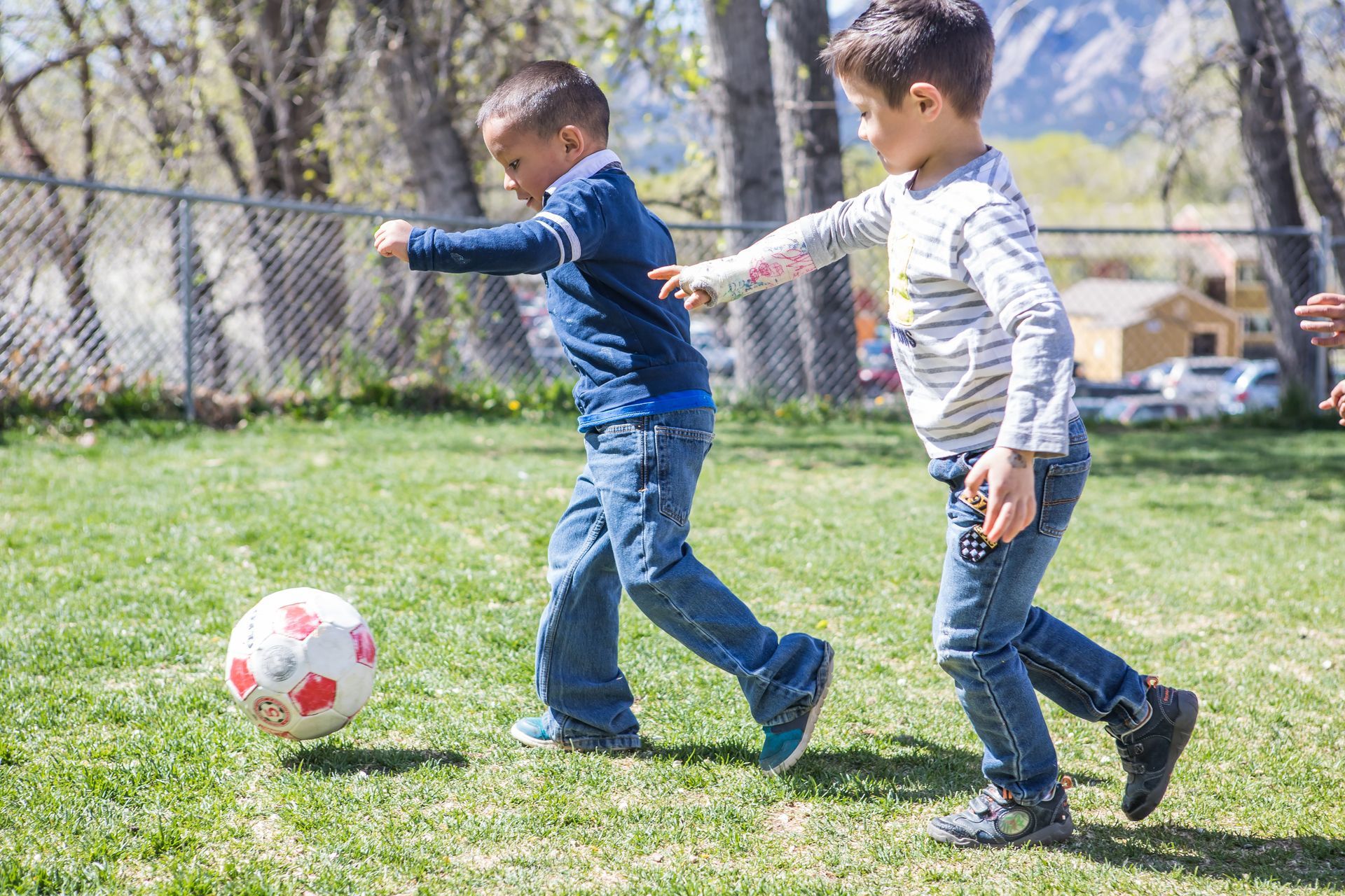Two young boys playing soccer on a grassy field. One kicks the ball while the other runs alongside.