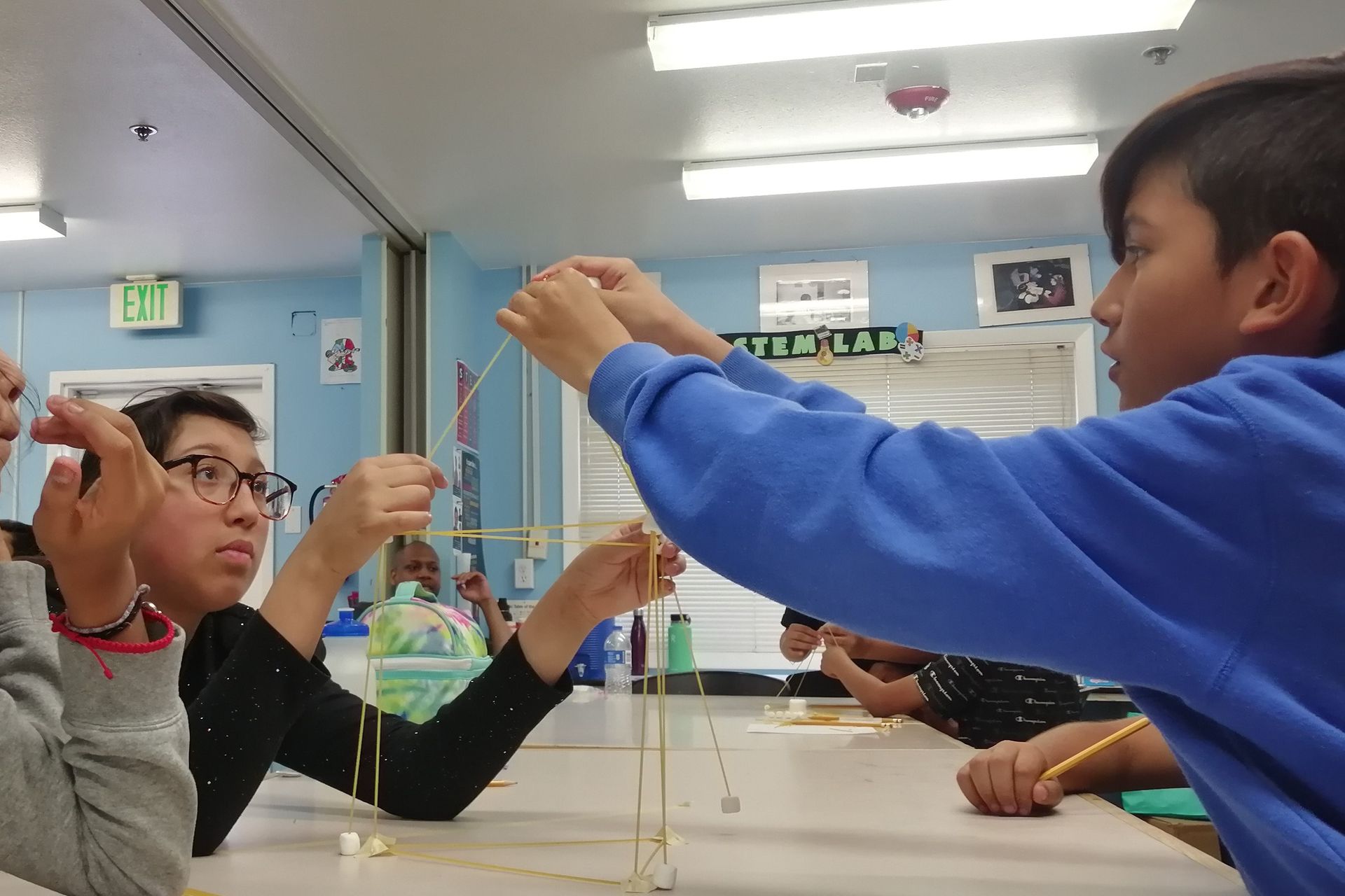 Students building a structure with spaghetti and marshmallows in a classroom, focused on the construction process.