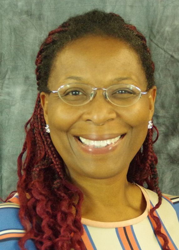 Smiling Black woman with glasses, auburn braids, wearing a striped top.
