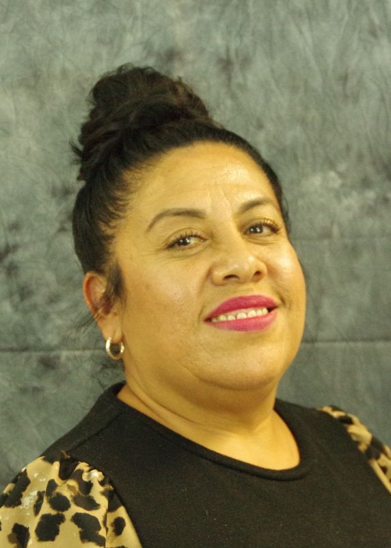 Woman with dark hair in a bun smiles, wearing a black top with a leopard print sleeve against a grey background.