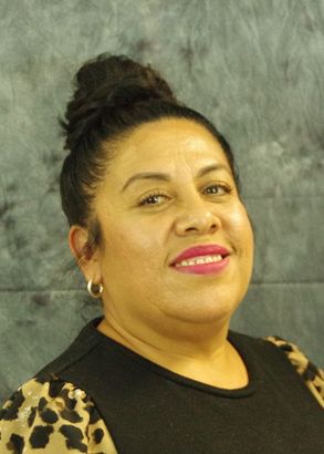 Woman with dark hair in a bun smiles, wearing a black top with a leopard print sleeve against a grey background.