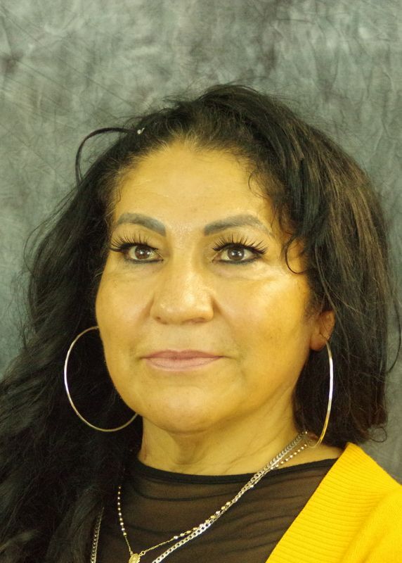 Woman with dark hair, hoop earrings, and yellow sweater smiles.