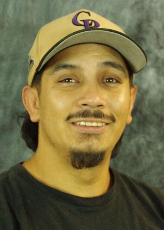 Man wearing a Colorado Rockies hat smiles, black shirt, dark hair and goatee, indoor.
