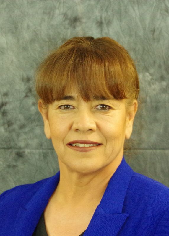 Woman with short, auburn hair and a blue blazer smiles, looking at the camera.