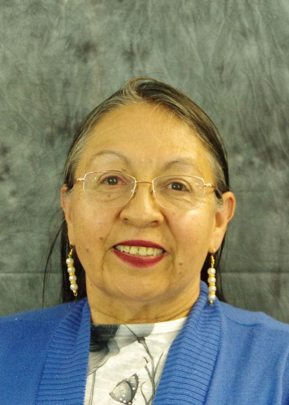 Smiling older woman with glasses and pearl earrings, wearing a blue sweater.