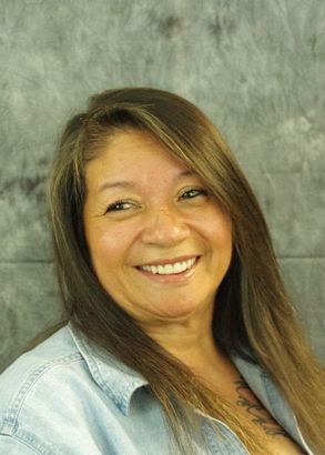 Smiling woman with long brown hair and a denim shirt.