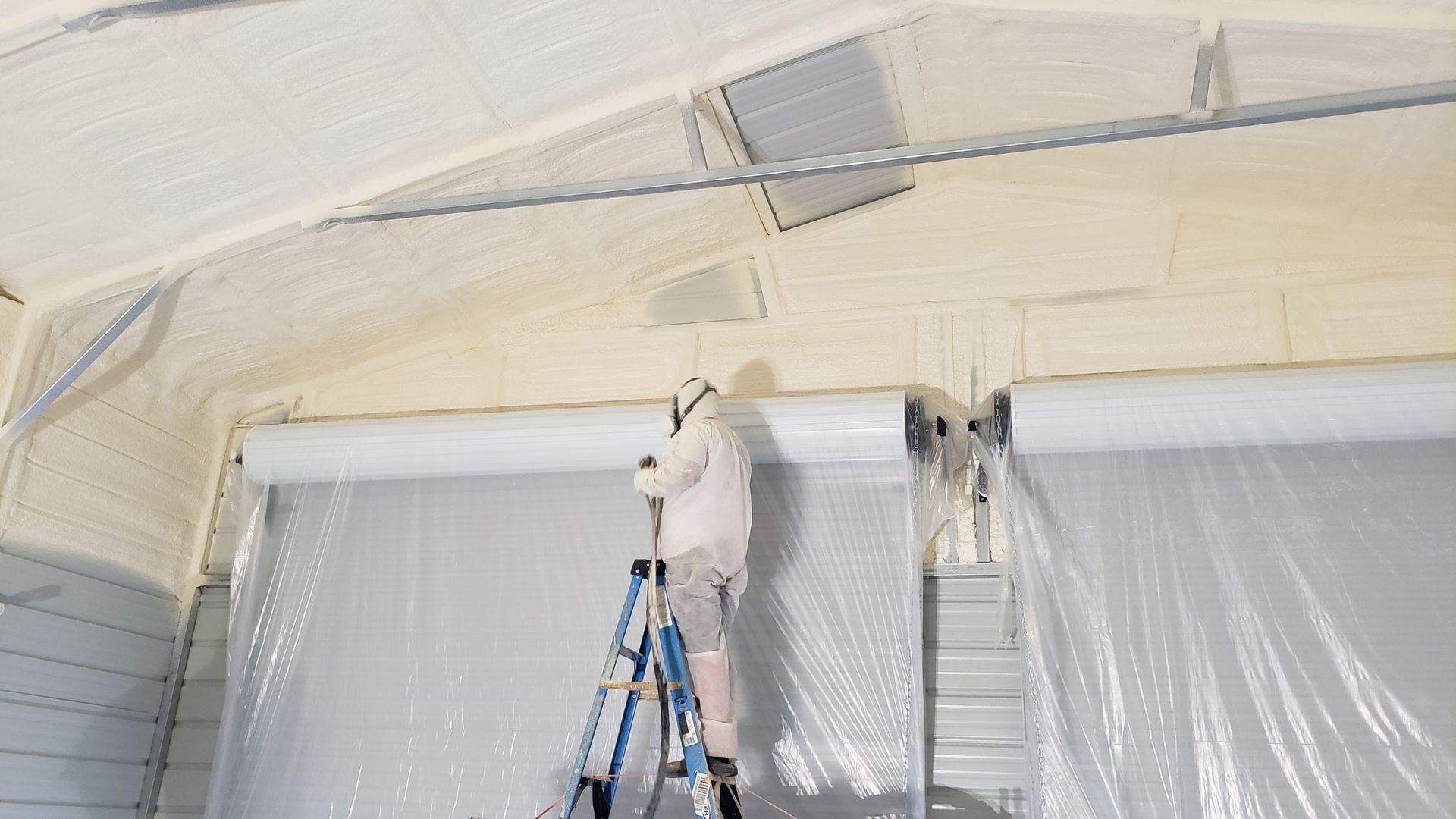 A man is standing on a ladder painting the ceiling of a building.