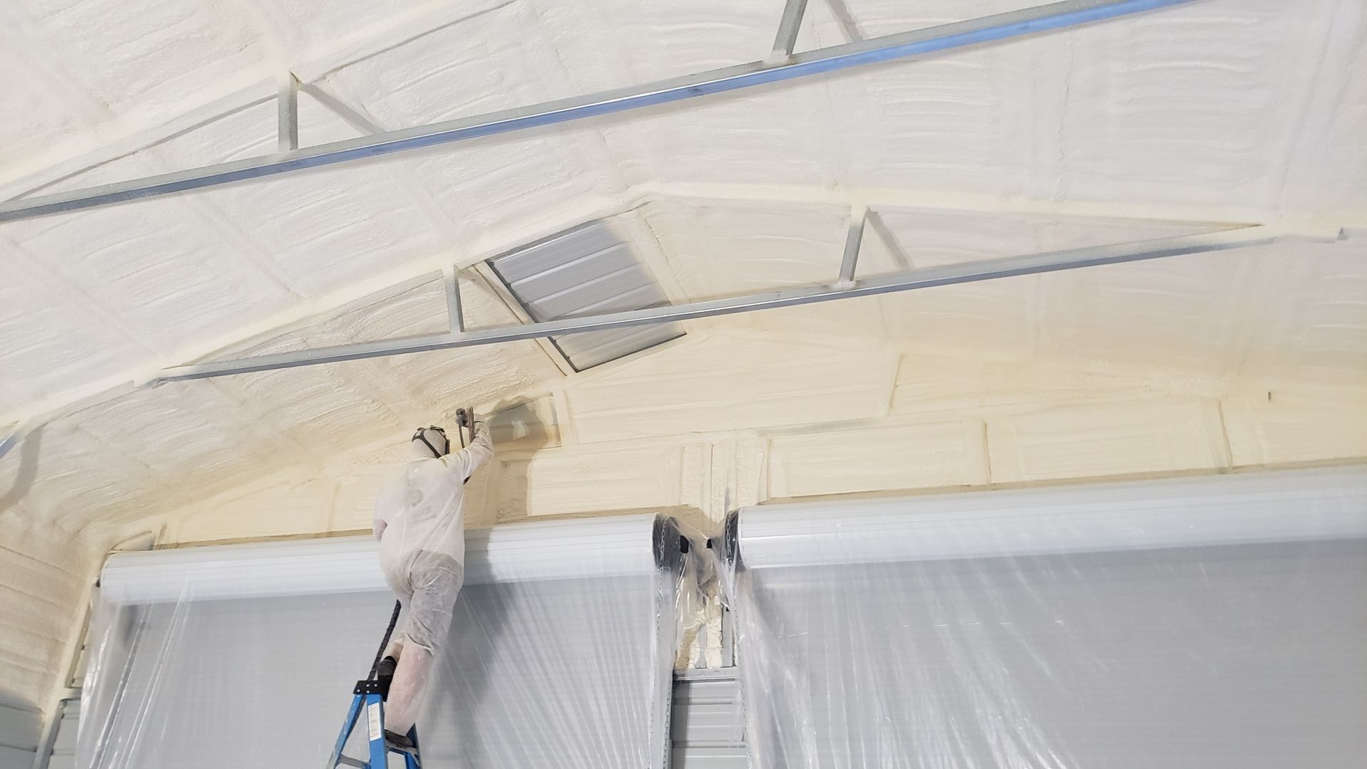 A man is standing on a ladder painting the ceiling of a building.