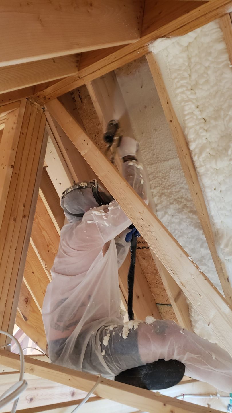 A man is spraying foam on the ceiling of a building.