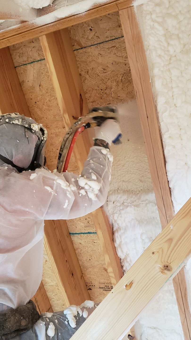 A man is spraying foam on the ceiling of a house.
