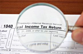 Man using magnifying glass on income tax return form