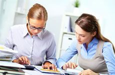 Portrait of two young businesswomen working with calculators in office