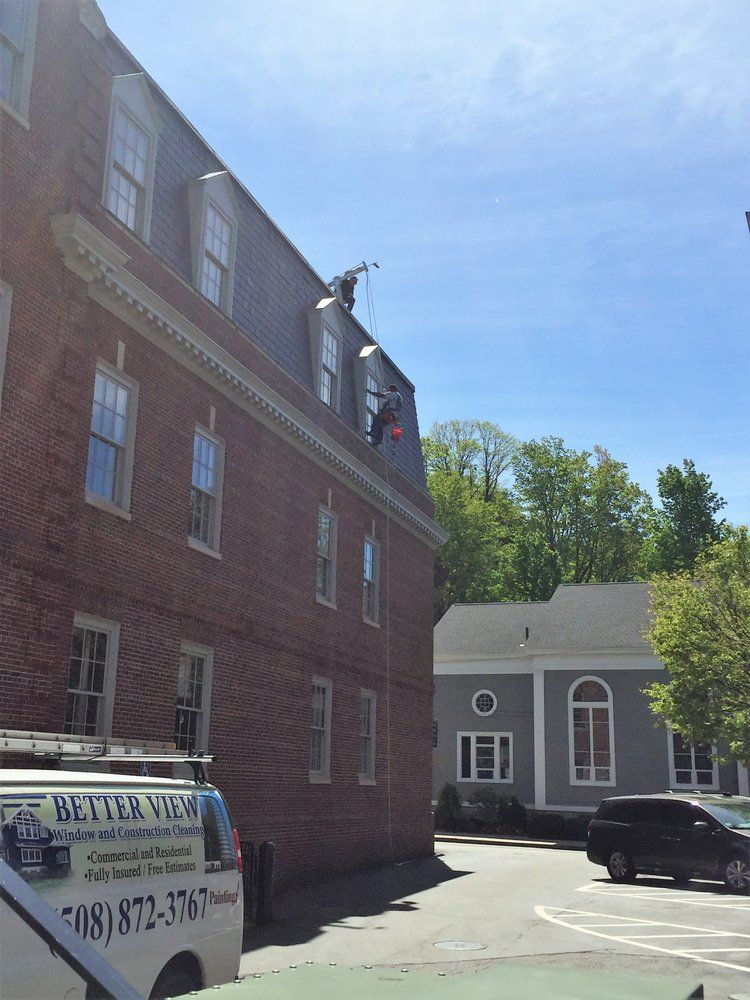 Brick building with a hanging sign, a white garage-like building, and a parked black car in a sunny lot