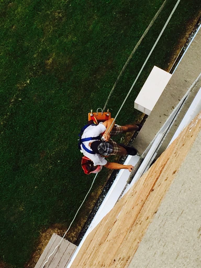 Climber in helmet and harness scaling a steep outdoor rock wall with ropes and gear