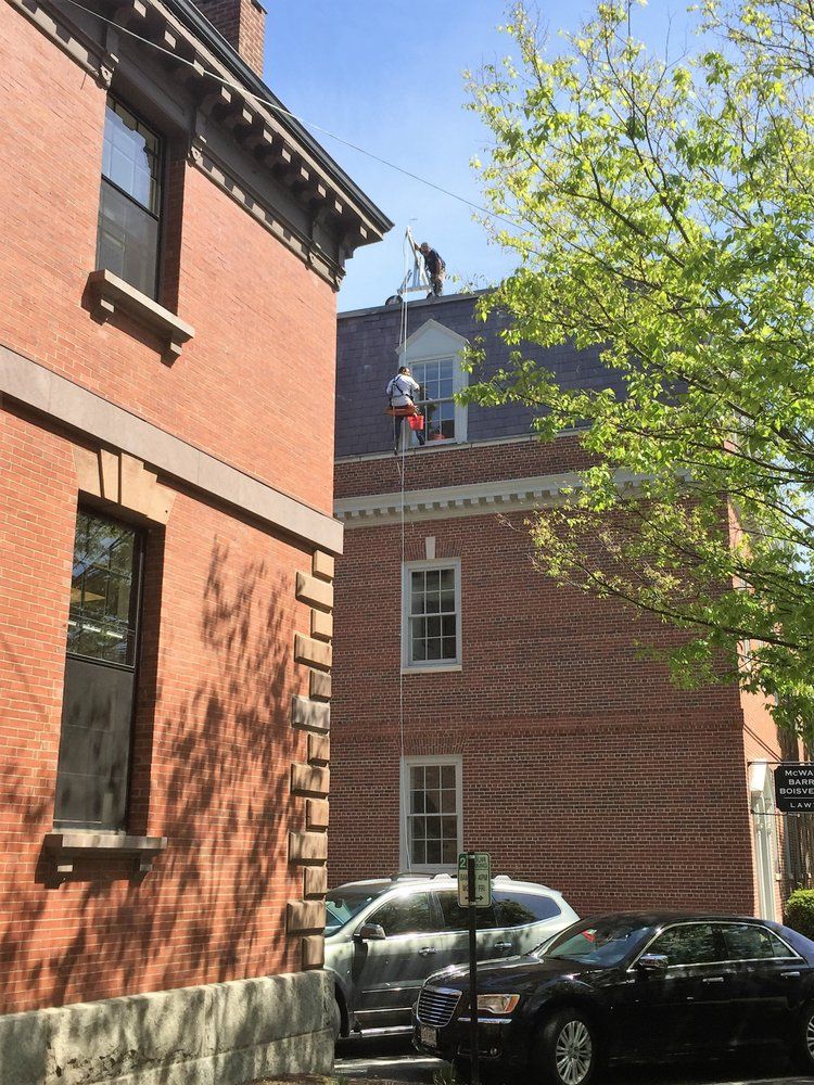 Narrow street between red brick buildings with parked cars and a leafy tree in sunlight.