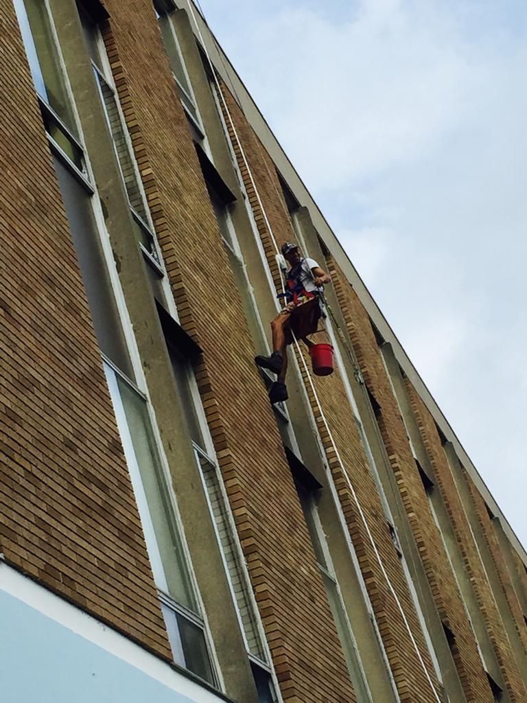 Window cleaner rappelling down a tall brick building with a red bucket