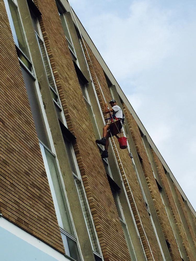 Two window washers suspended on ropes cleaning a tall brick building facade