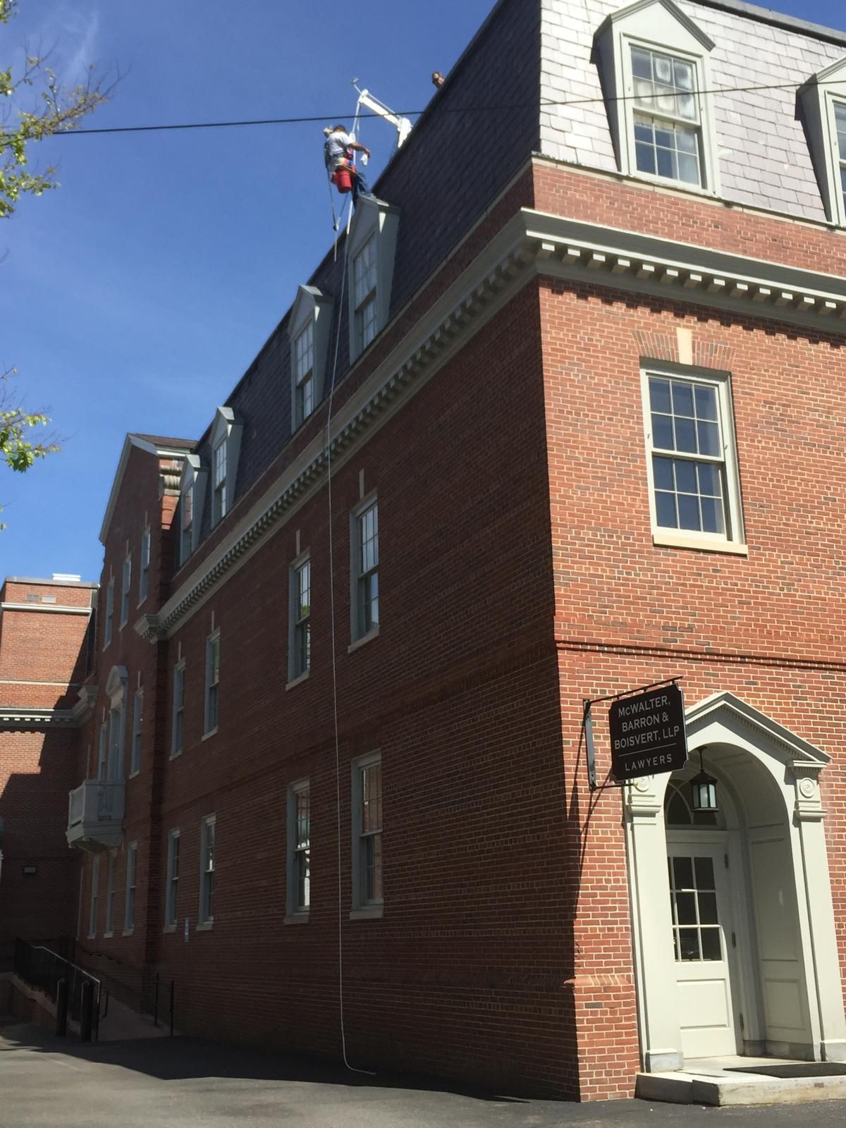 Red-brick building with white-trimmed windows and a white entryway under a blue sky.