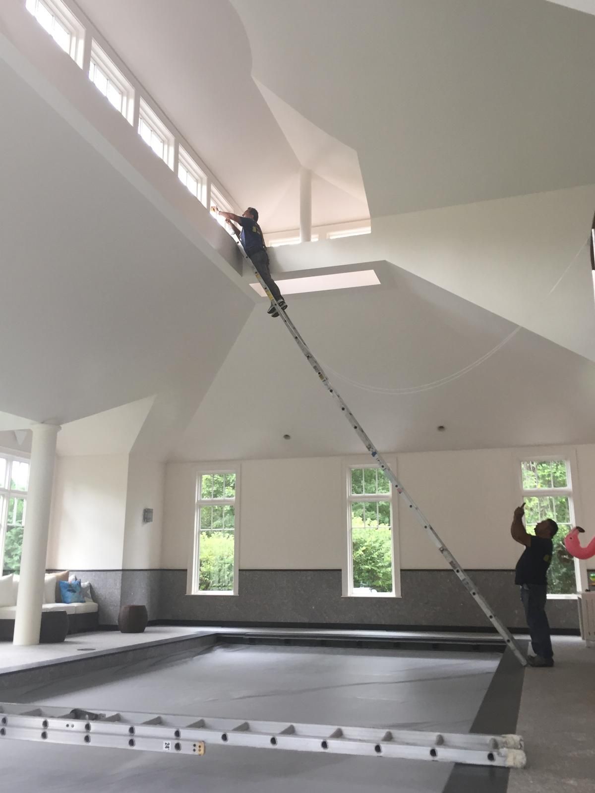 Workers installing a large suspended ceiling panel in a bright hall using a long pole