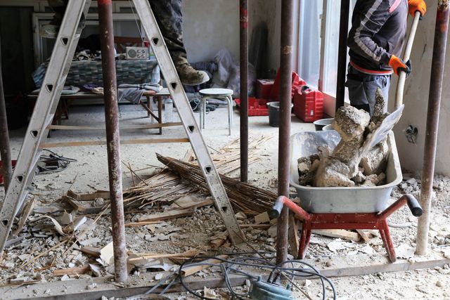 Construction workers clearing debris in a room with ladders and tools.