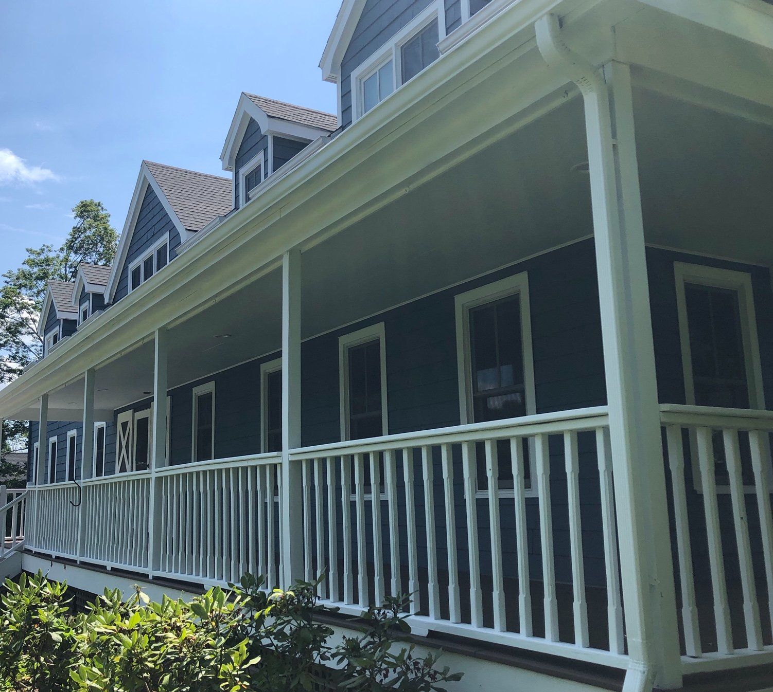 Blue house with white trim, including a porch with a white railing. Overhanging porch roof and gutters are also white.