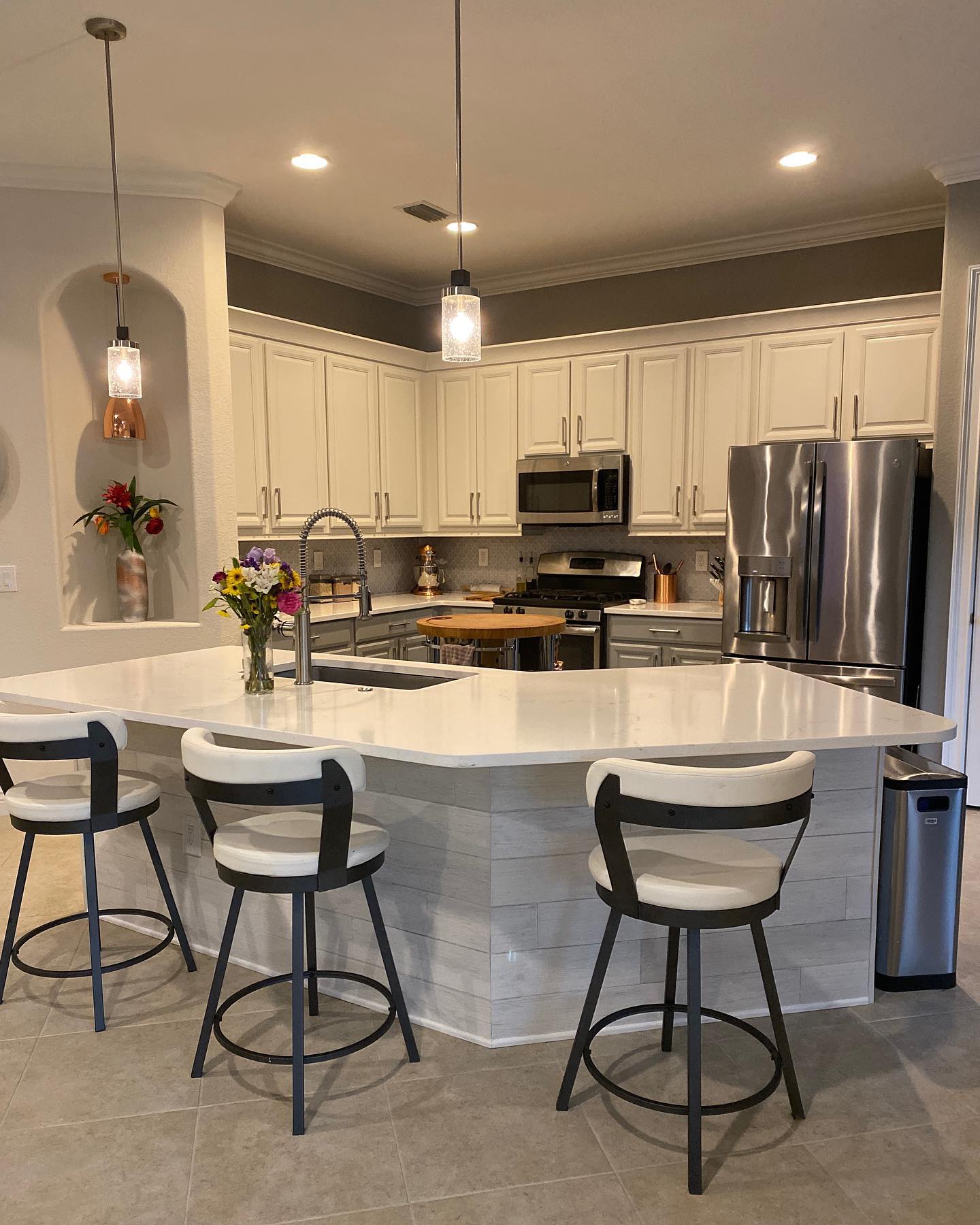 Kitchen with white cabinets, island with seating, stainless steel appliances, and pendant lights.