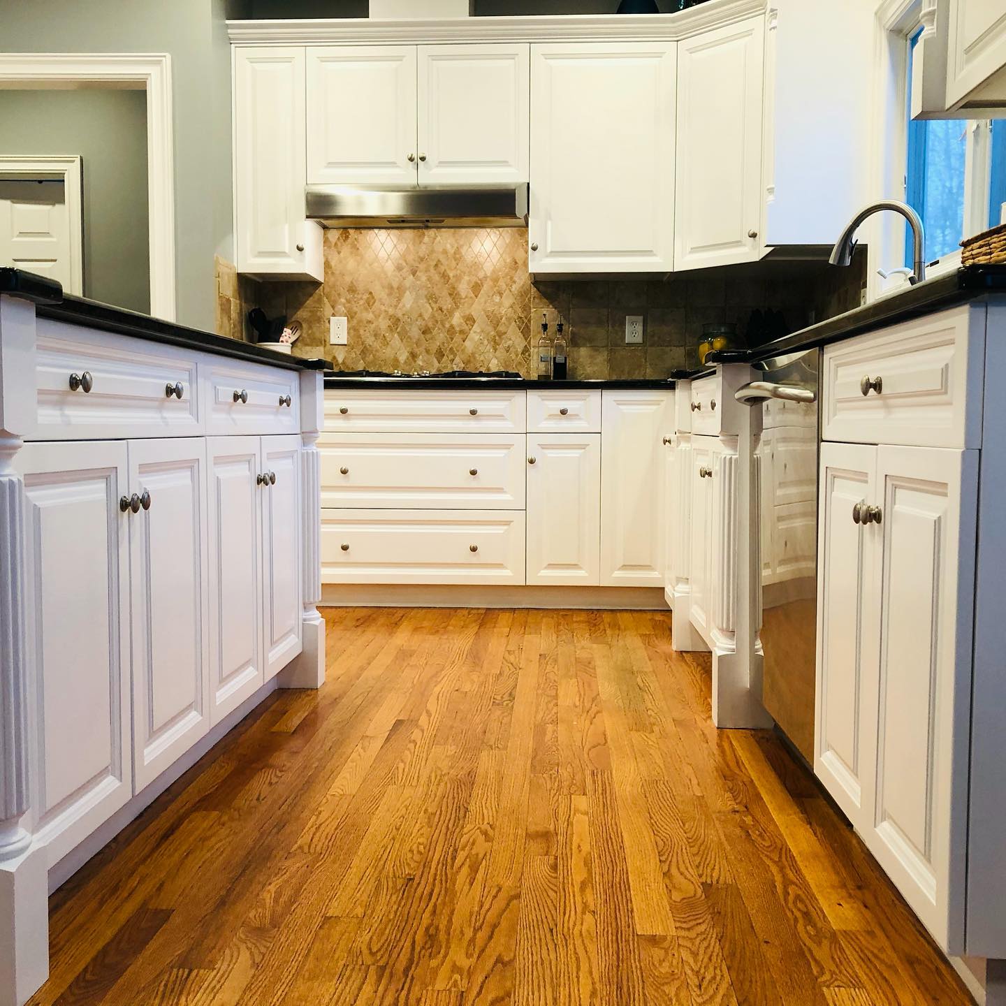 White kitchen cabinets with a black countertop, stainless steel appliances, and hardwood floors.