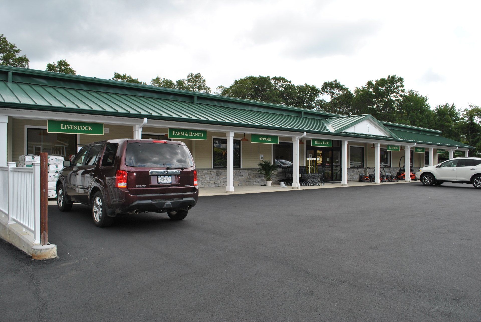 A commercial strip mall with a dark SUV parked in front. The building has a green roof and white columns.