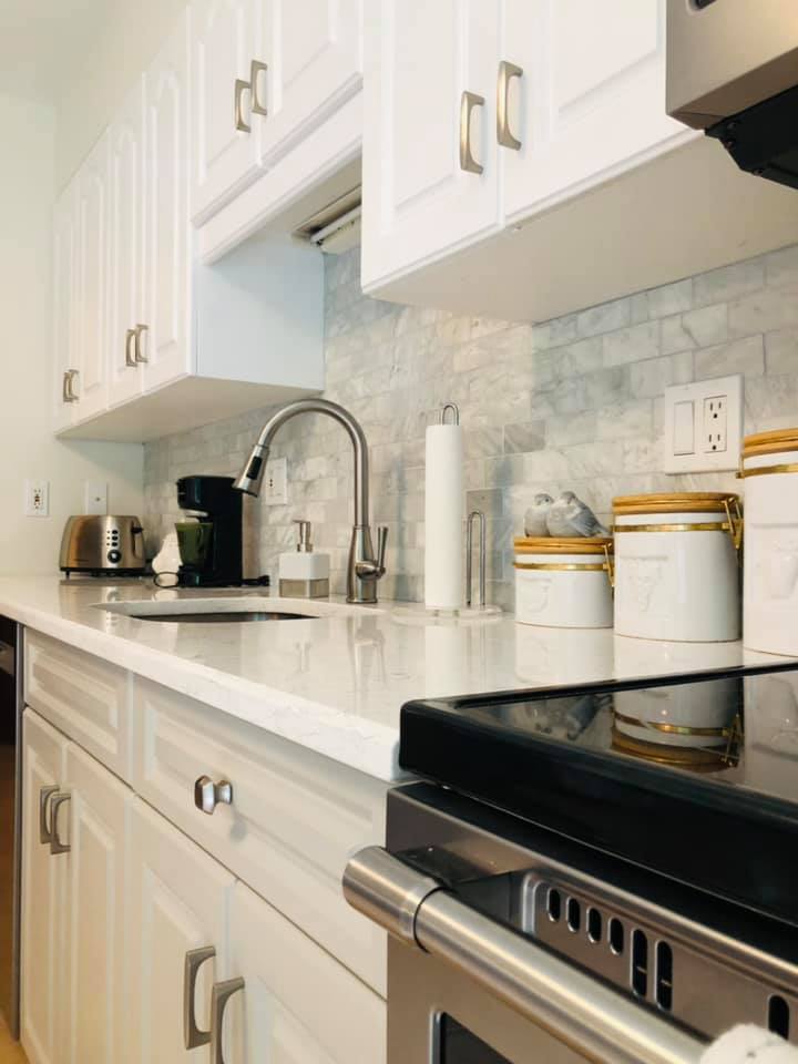 White kitchen with a stainless steel oven, countertops, and cabinets. There's a sink, backsplash, and appliances like a coffee maker and toaster.