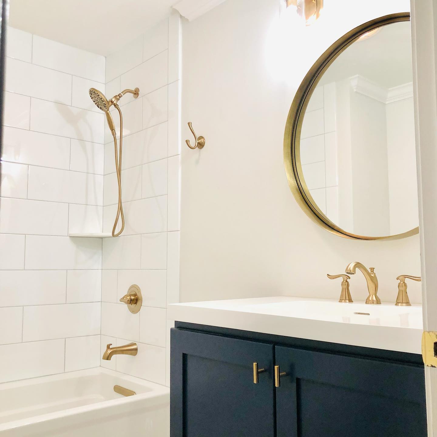 A modern bathroom with a white subway tile shower, navy blue vanity, and gold fixtures.