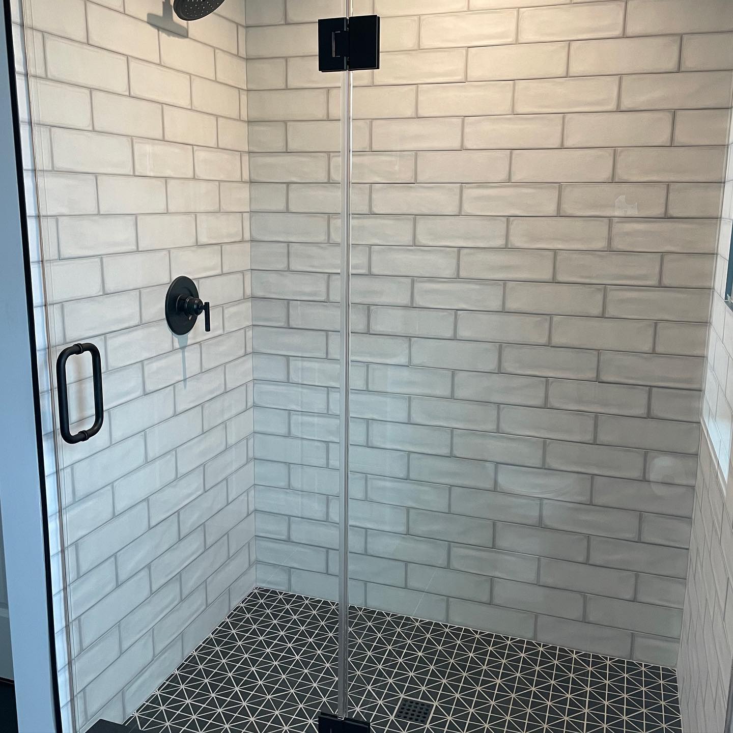 A modern shower with white subway tile walls, a pebble tile floor, and a glass door with black hardware.