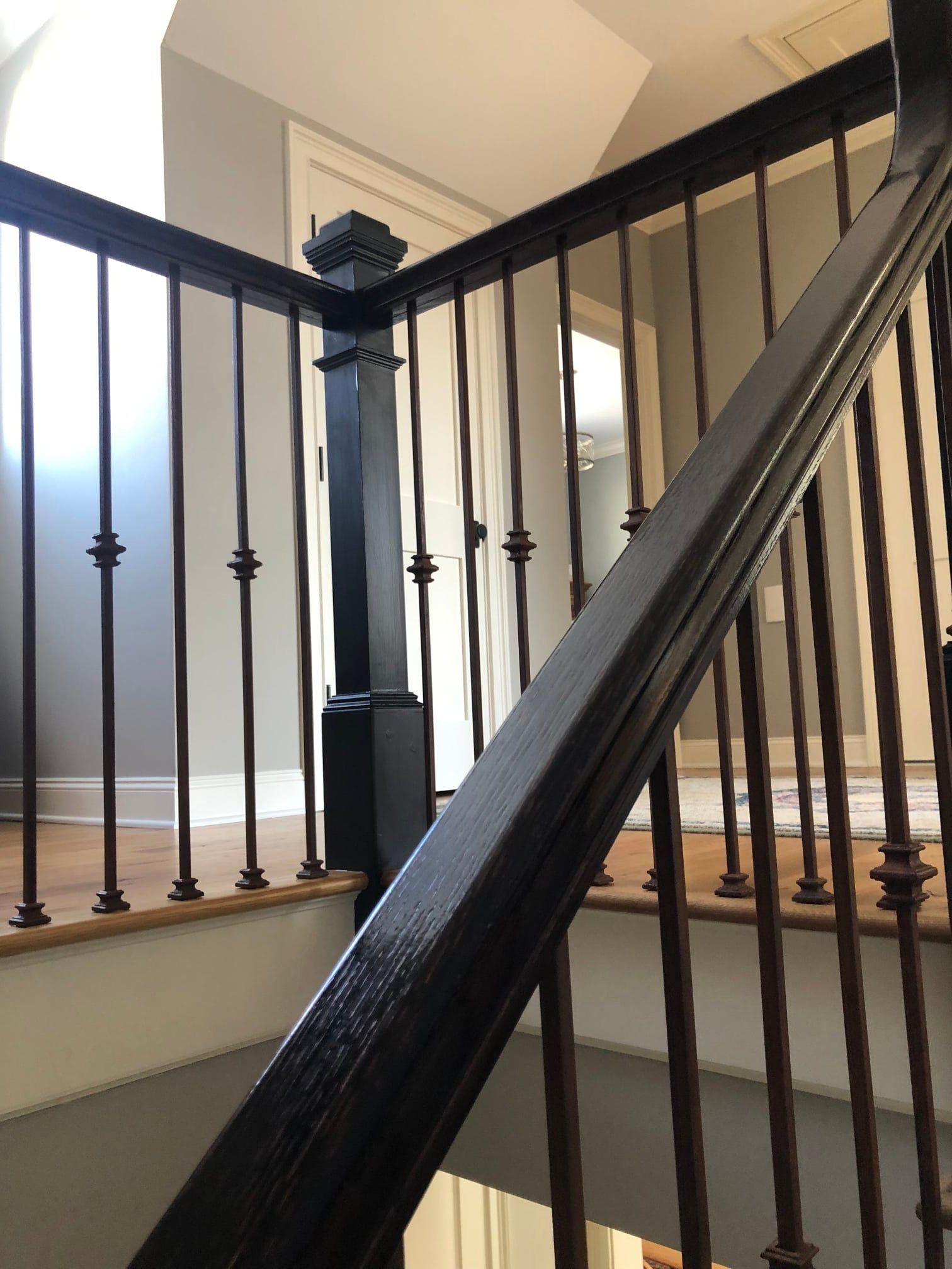 Black wooden staircase with wrought iron spindles; a dark-colored railing is visible, with wooden steps leading down.