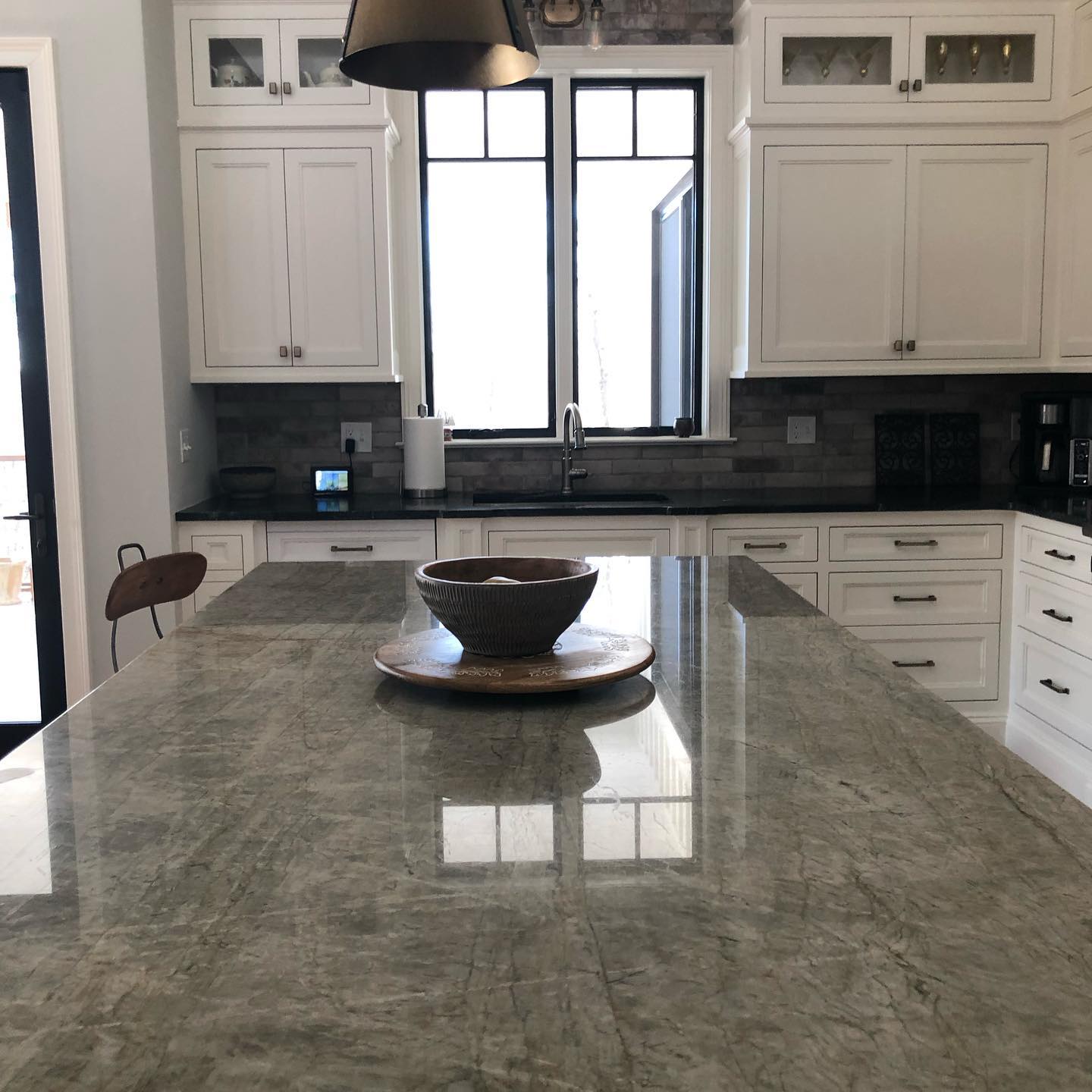 Kitchen with white cabinets, a large granite countertop island, and a window above the sink. A bowl sits on the island.