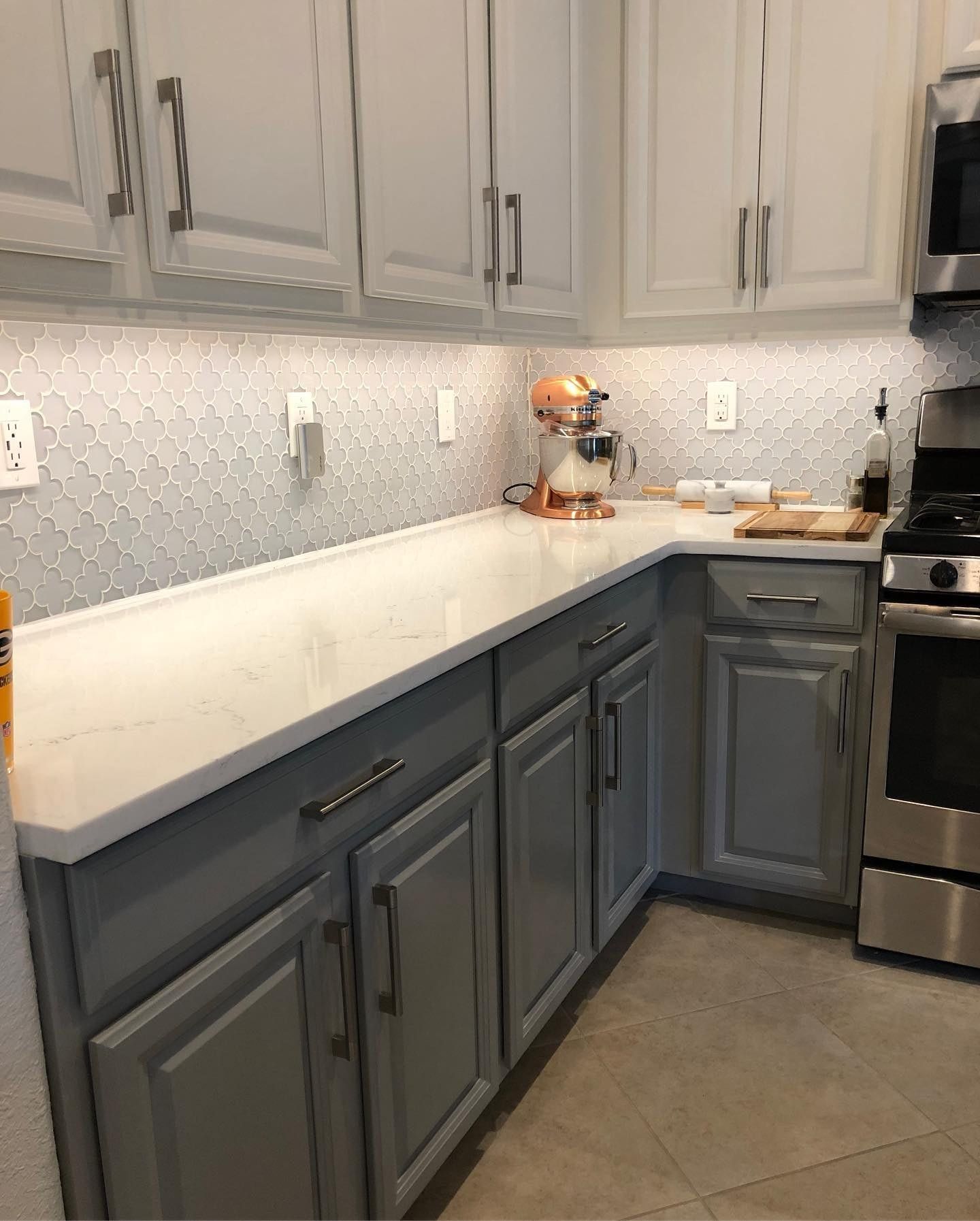 Gray and white kitchen with light-colored counters, cabinets, and a mosaic backsplash. A stand mixer and stove are visible.