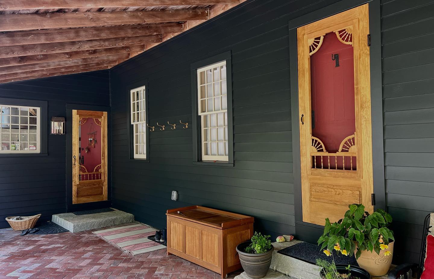 Exterior of a house with dark gray siding, tan wooden doors, and a covered porch. Two screen doors and two windows are visible.