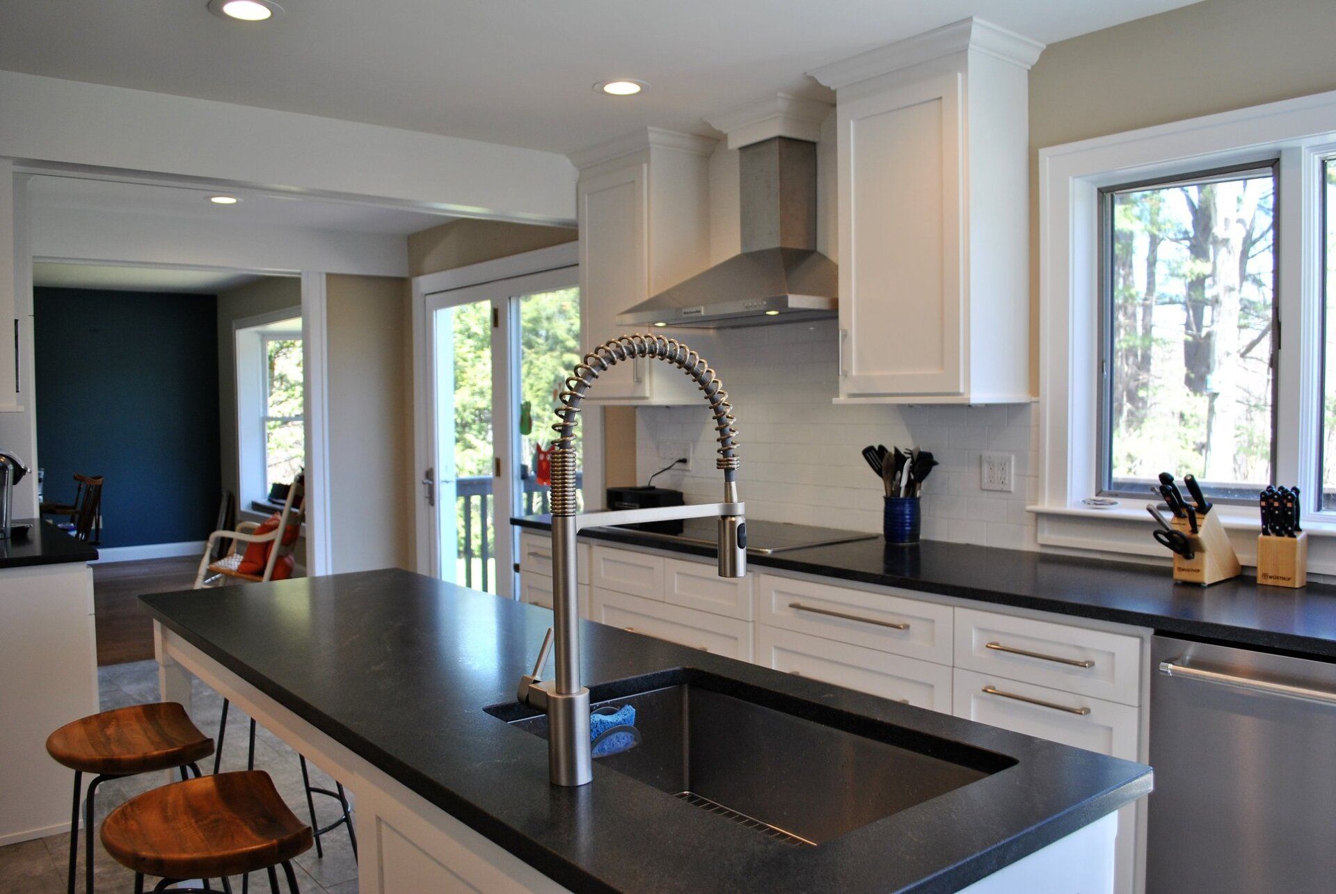 Modern kitchen with white cabinets, dark countertops, and stainless steel appliances. An island with a sink and a faucet dominates the foreground.