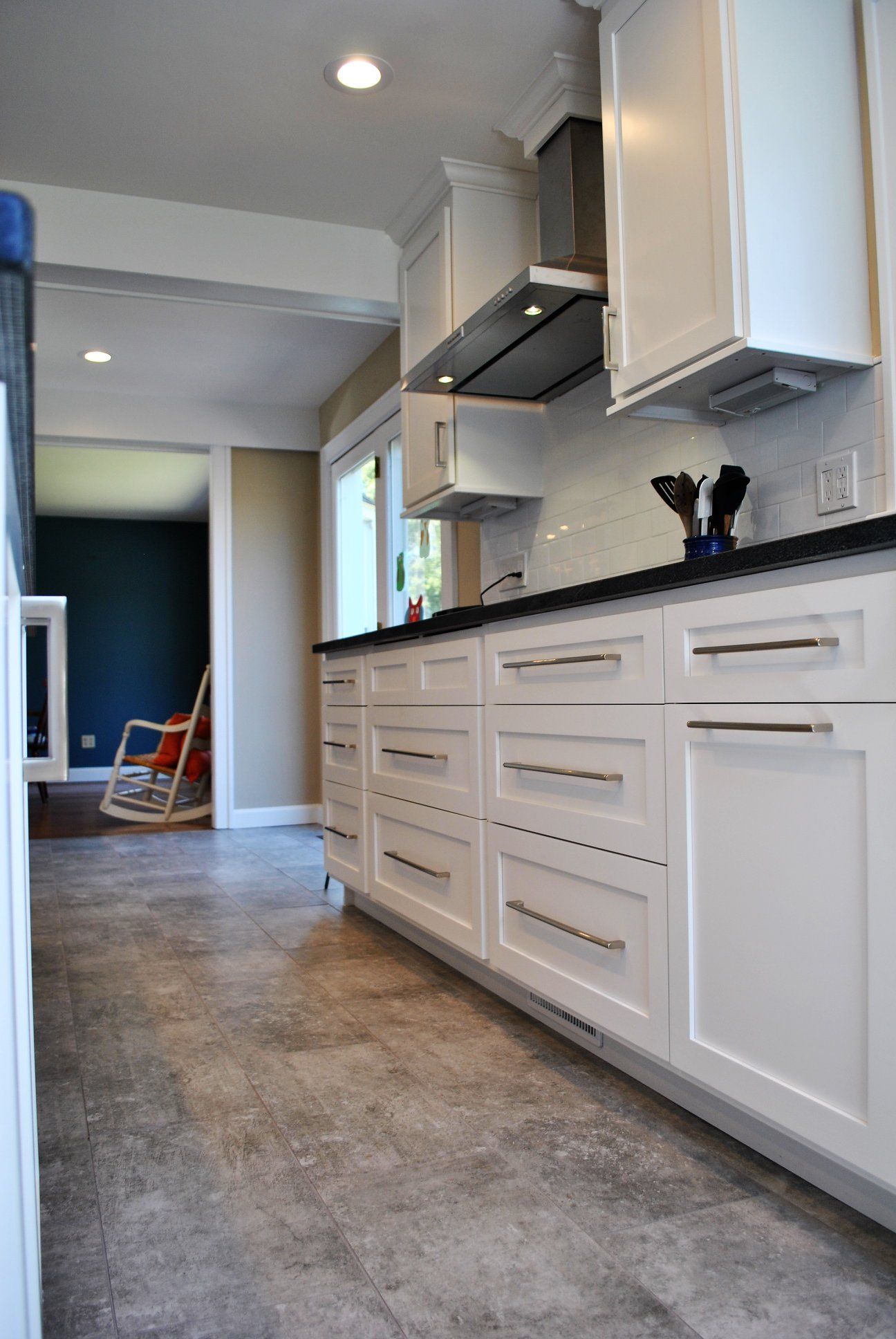 White kitchen cabinets with silver hardware and black countertops. Gray flooring leads to a doorway and a blue wall.