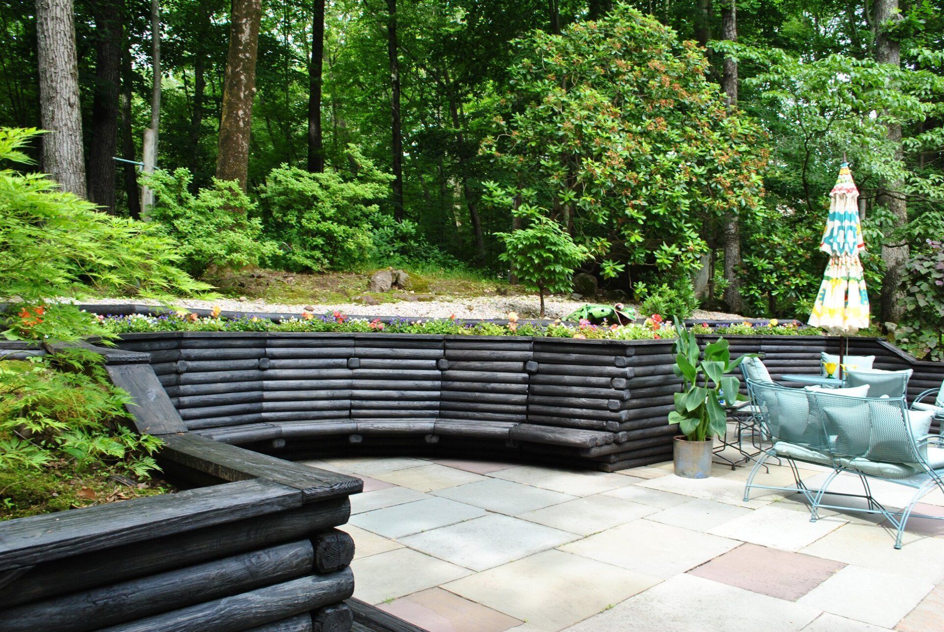 Outdoor patio with a curved wooden bench and colorful umbrella; trees in the background.
