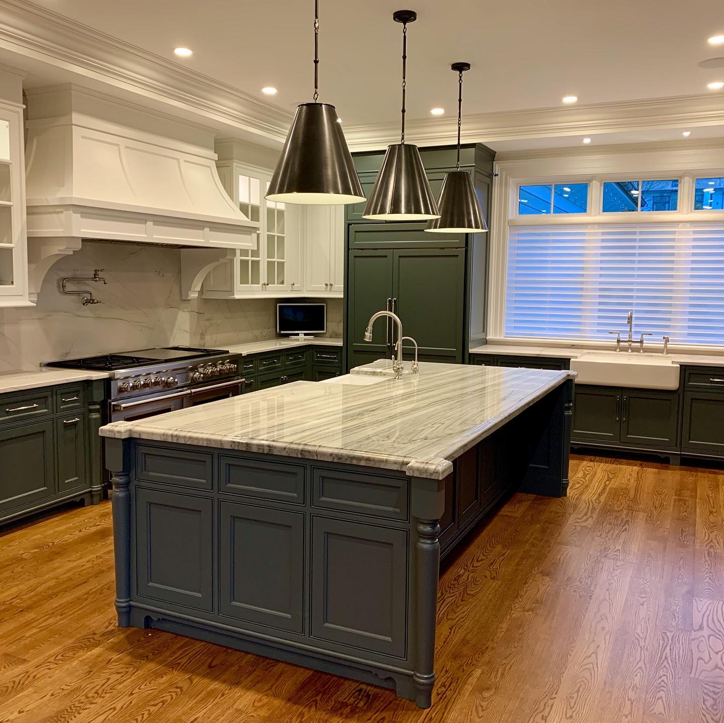 Spacious kitchen with a large gray island, dark green cabinets, white countertops, and three hanging black pendant lights.