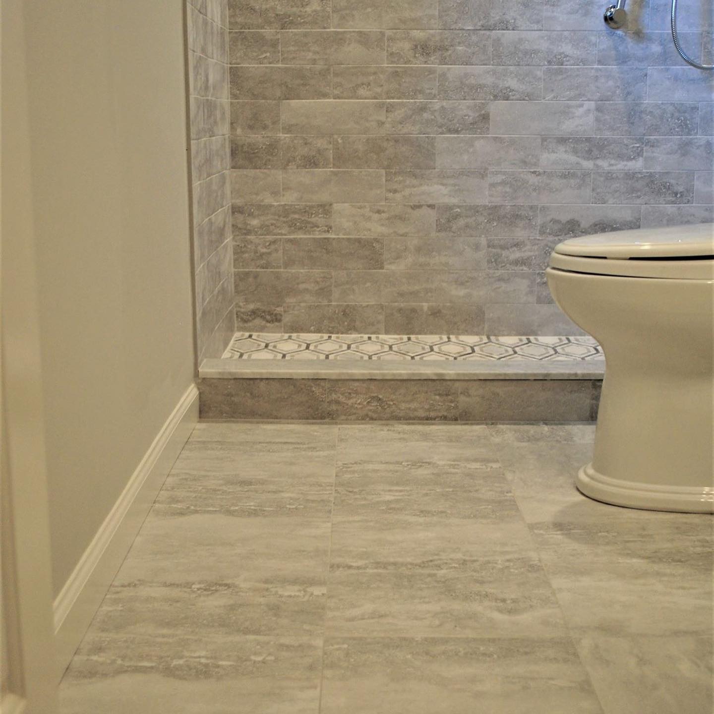 A bathroom with gray tile flooring and a shower, a white toilet, and light gray walls.