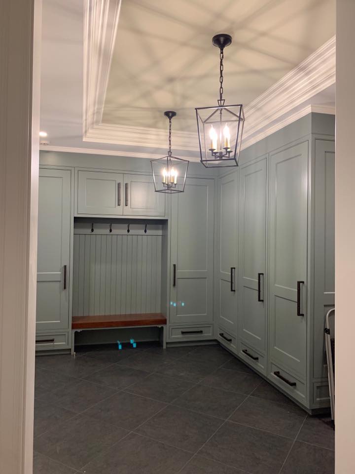A mudroom with sage green cabinets, dark hardware, and two pendant lights. A built-in bench and coat rack sit in the center.