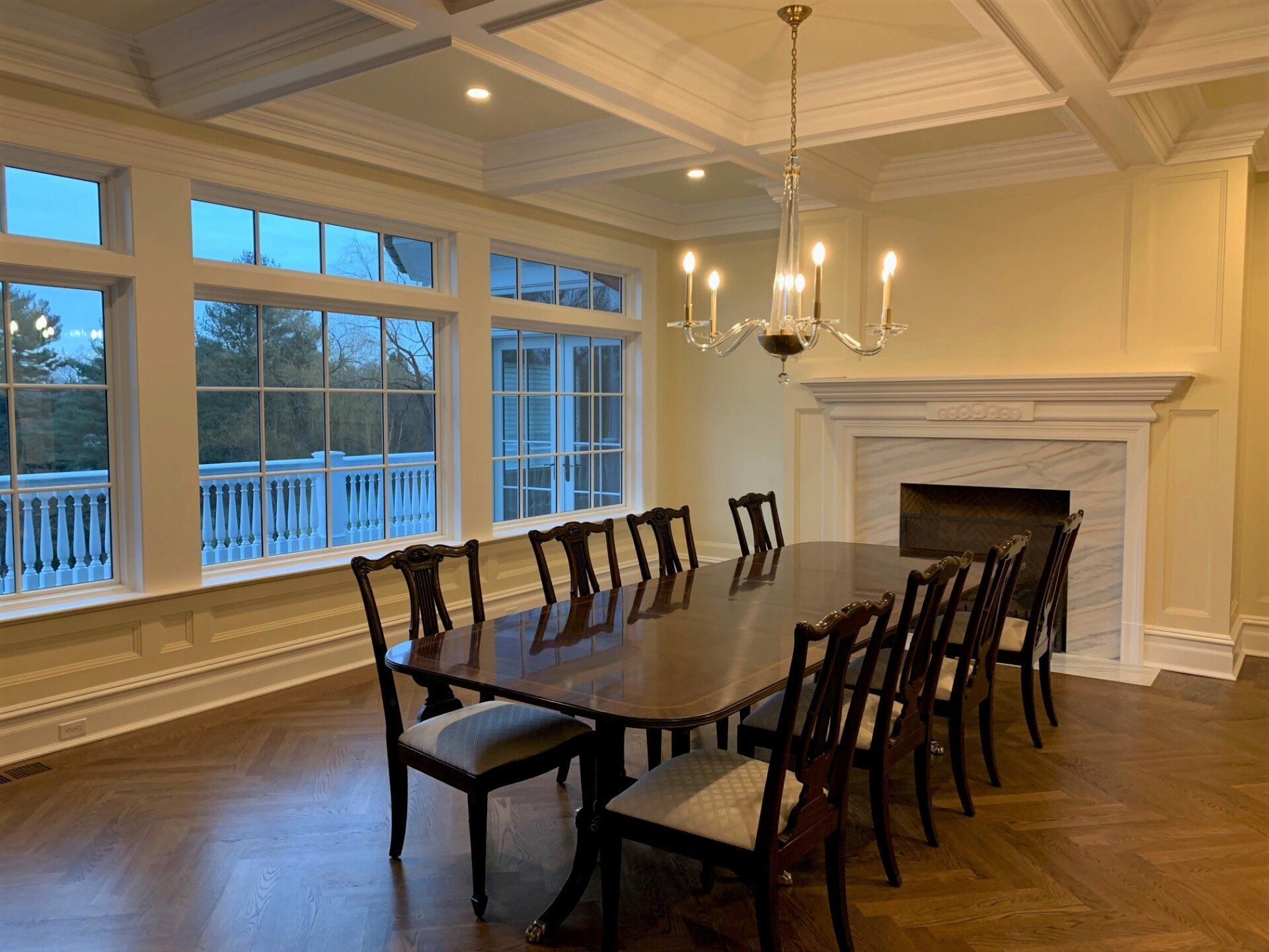 Formal dining room with large windows overlooking a deck.  A long table is set for a gathering, with ten chairs around it.