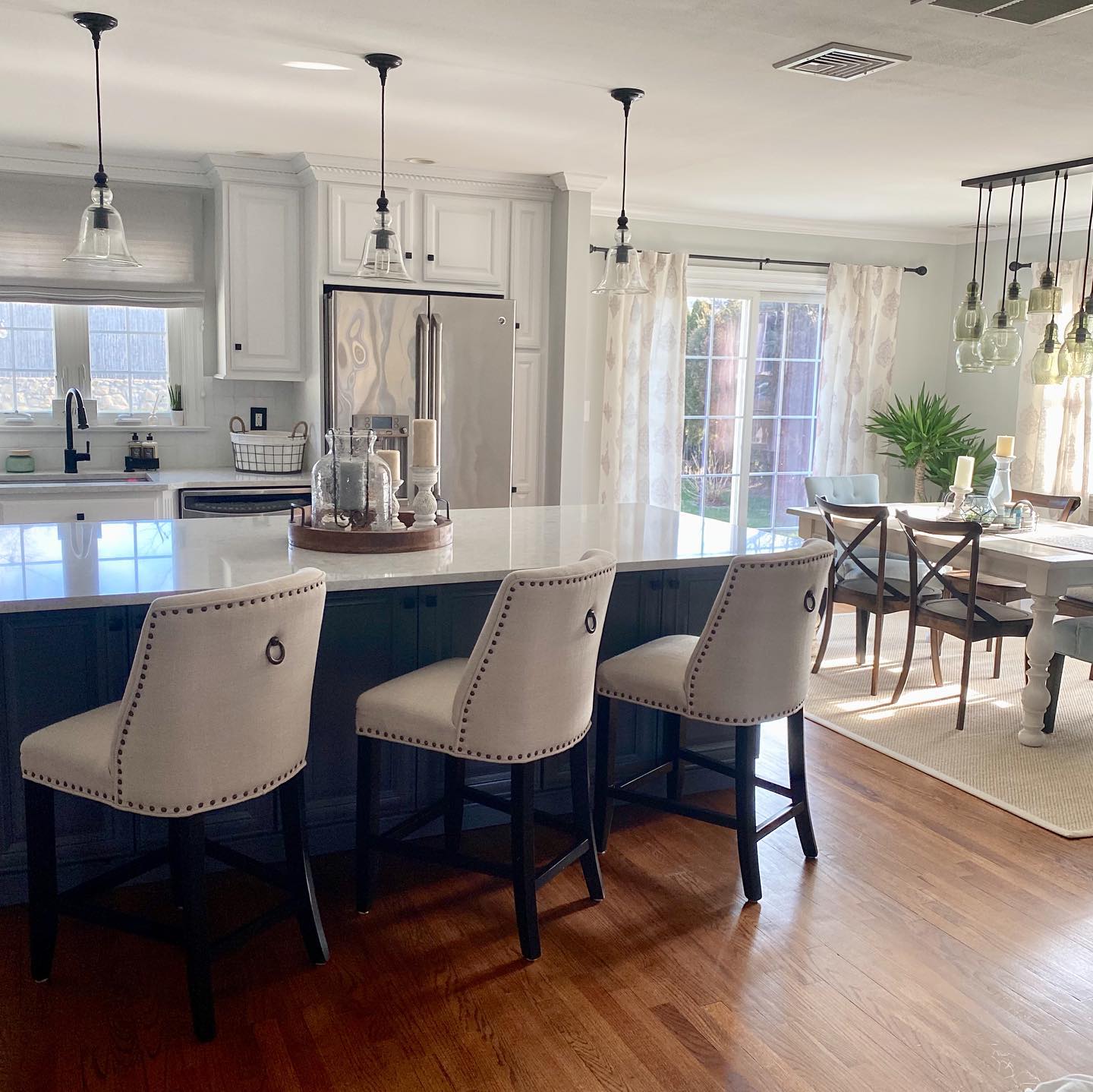 Spacious kitchen with an island, bar stools, and a dining area. Features neutral colors, pendant lights, and a sunny atmosphere.