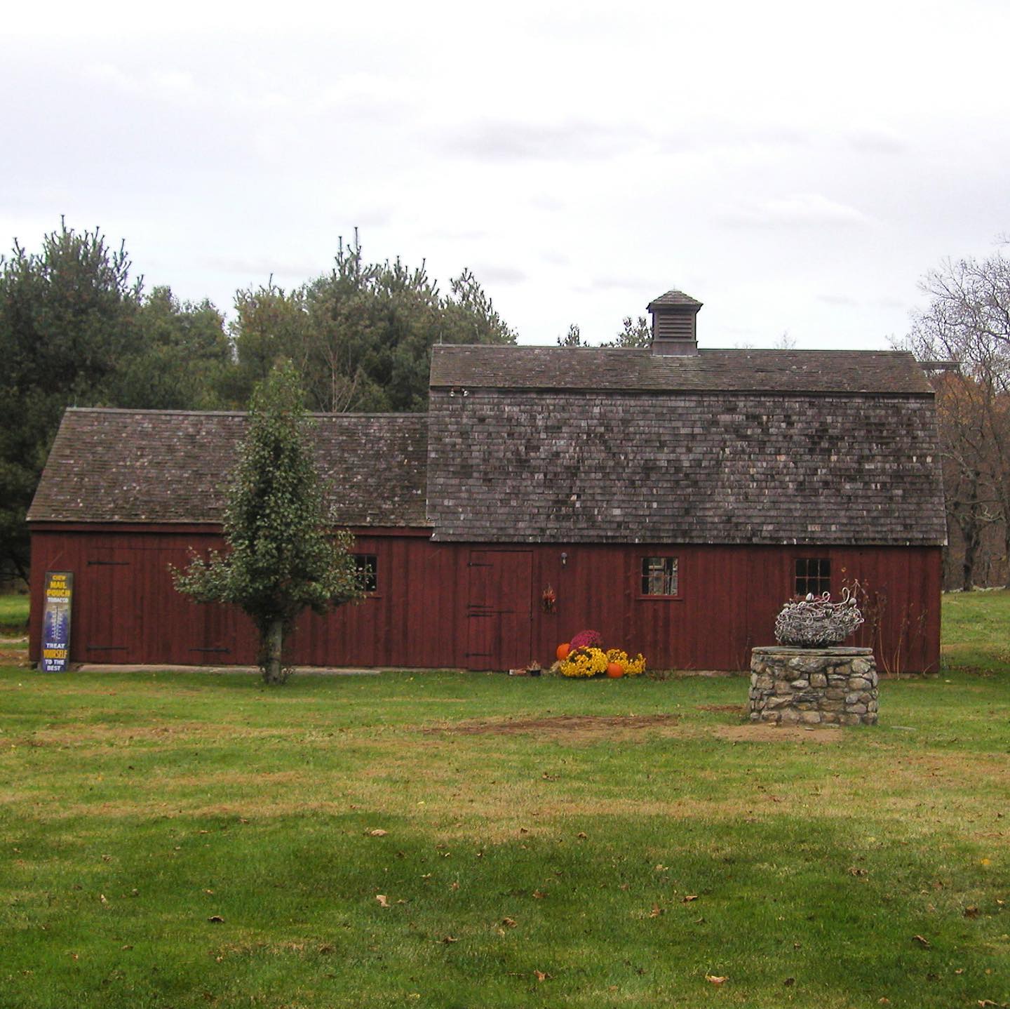 Red barn with a weathered gray roof, set in a grassy field with trees in the background.
