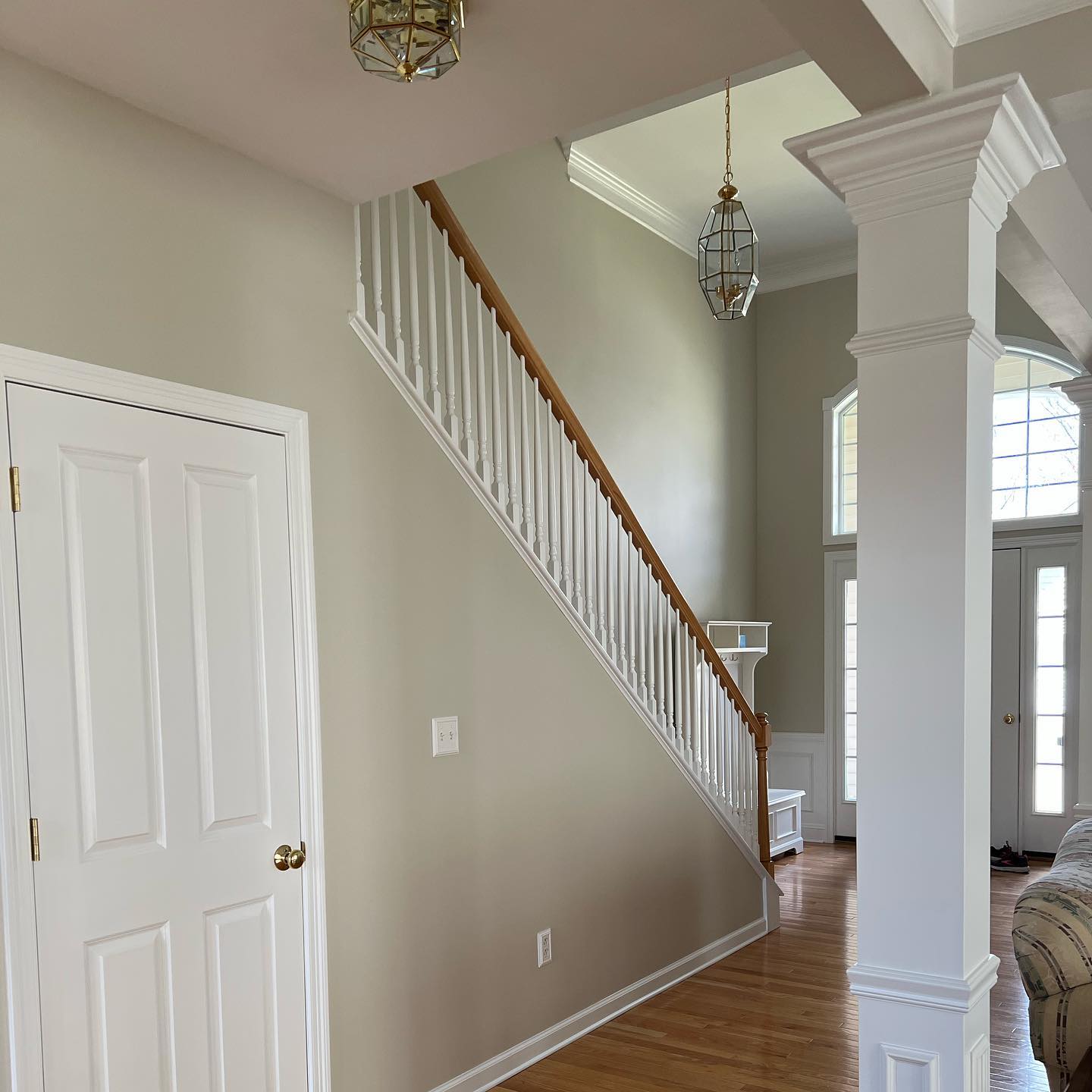 Interior view of a home with a staircase, white door, and columns. The walls are painted a neutral color, and the floors are hardwood.