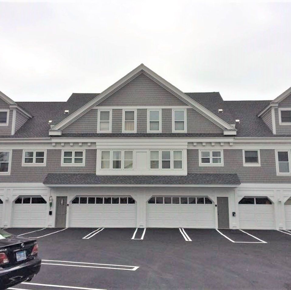 Gray townhomes with white garage doors and parking spaces in front, under a cloudy sky.