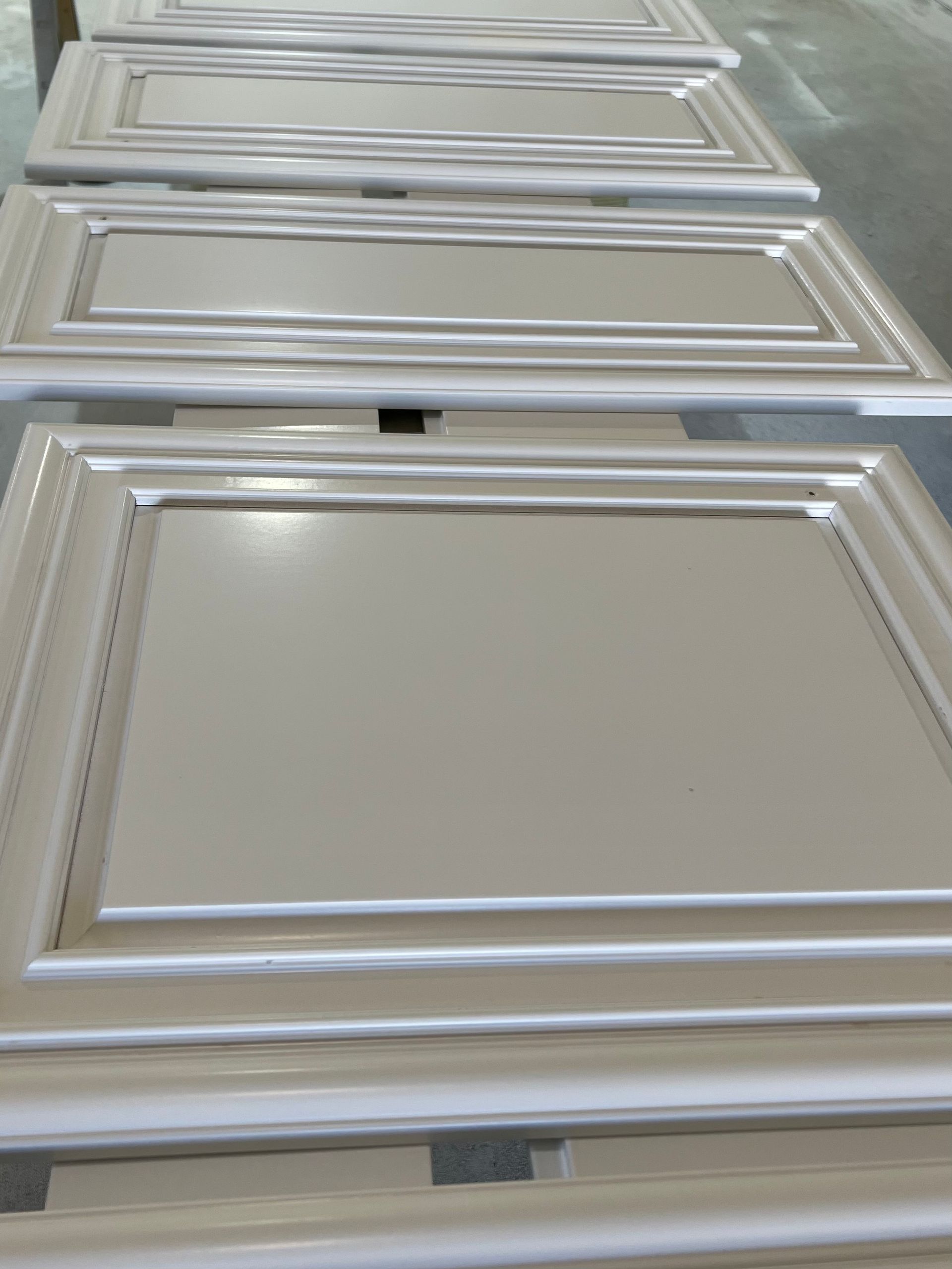 Painted cabinet doors laid out in rows, light neutral color.