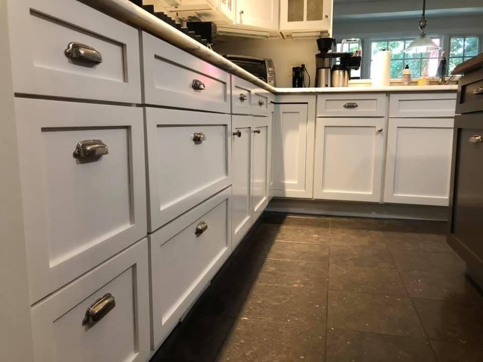 White kitchen cabinets with silver hardware and a dark brown floor.