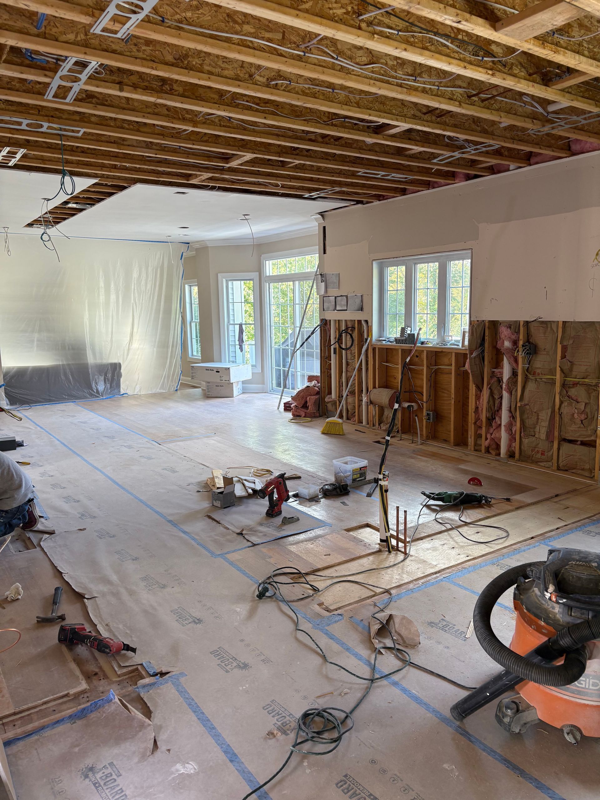 Renovation site with exposed ceiling joists, stripped walls, debris, and a saw on the floor